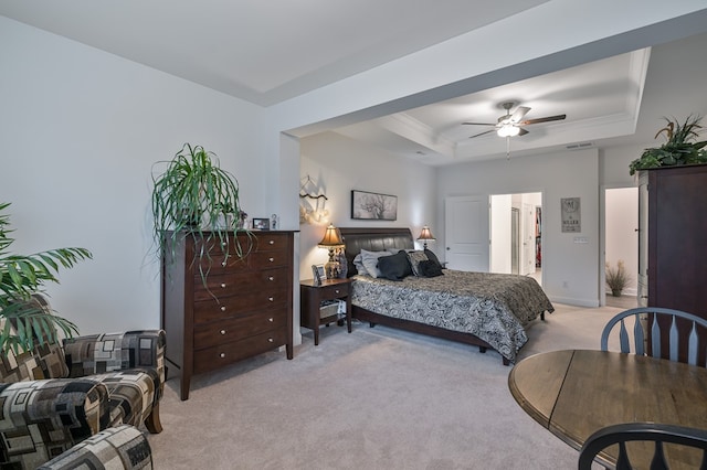 bedroom featuring light carpet, a tray ceiling, ensuite bath, and ceiling fan