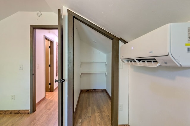 hallway featuring light hardwood / wood-style floors, an AC wall unit, and lofted ceiling