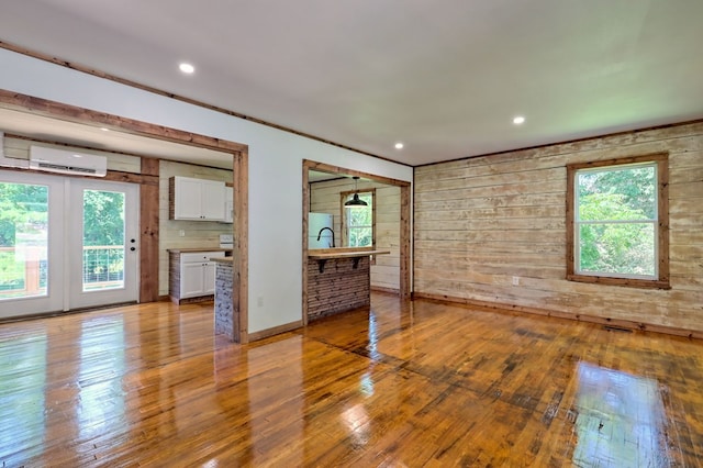 unfurnished living room with light hardwood / wood-style floors, a wall unit AC, and wood walls