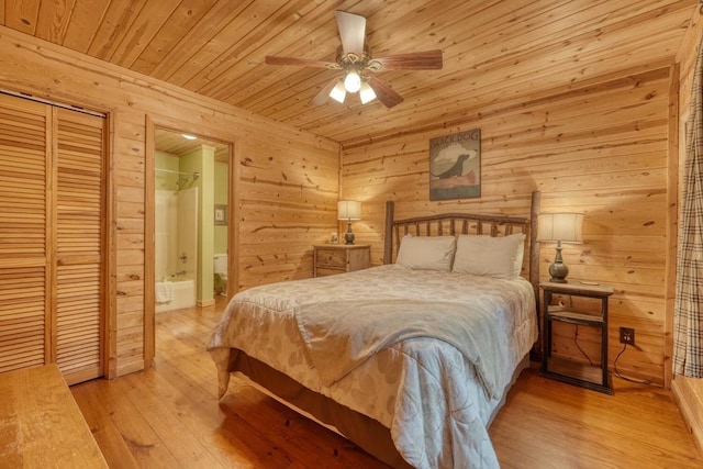 bedroom featuring wooden walls, ensuite bathroom, light wood-type flooring, and ceiling fan