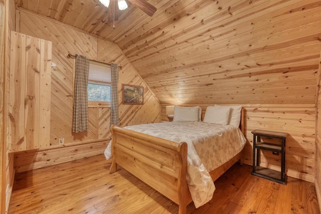 bedroom featuring lofted ceiling, wood ceiling, ceiling fan, light hardwood / wood-style flooring, and wooden walls