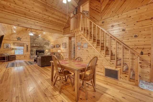 dining area featuring a fireplace, wooden walls, light wood-type flooring, and ceiling fan