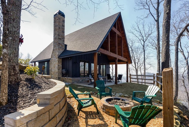 back of house with a shingled roof, a fire pit, a patio, fence, and board and batten siding