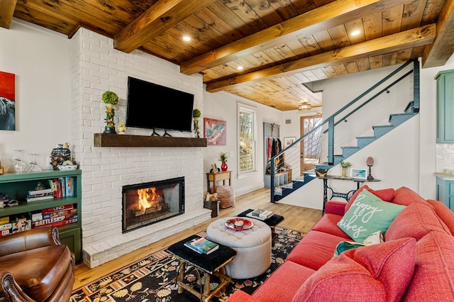 living area featuring beam ceiling, stairway, a brick fireplace, wood ceiling, and light wood-type flooring