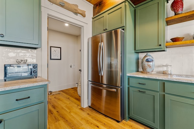 kitchen with green cabinetry, freestanding refrigerator, light countertops, open shelves, and backsplash