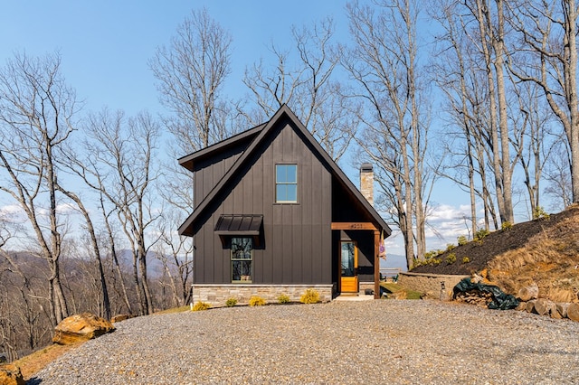 view of front of house with board and batten siding, stone siding, driveway, and a chimney