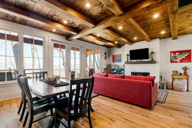 dining room featuring wooden ceiling, beamed ceiling, french doors, light wood-style floors, and a fireplace