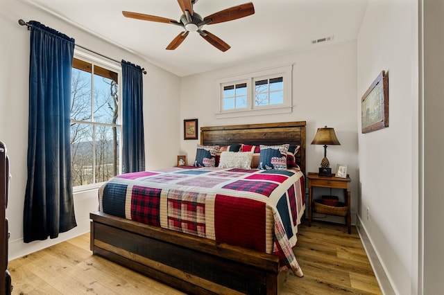 bedroom featuring a ceiling fan, wood finished floors, visible vents, and baseboards