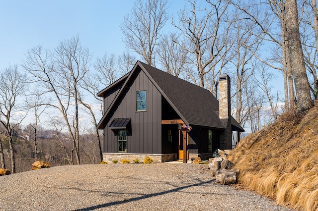 view of front facade featuring stone siding, a shingled roof, a chimney, and board and batten siding