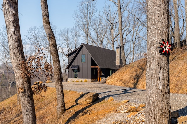 view of front facade with roof with shingles, a chimney, and board and batten siding