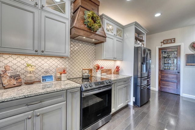 kitchen with appliances with stainless steel finishes, glass insert cabinets, custom exhaust hood, and light stone countertops