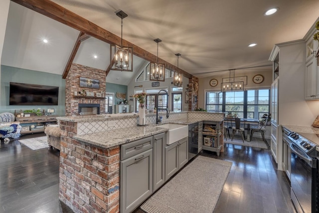 kitchen featuring electric range, light stone counters, open floor plan, pendant lighting, and a sink