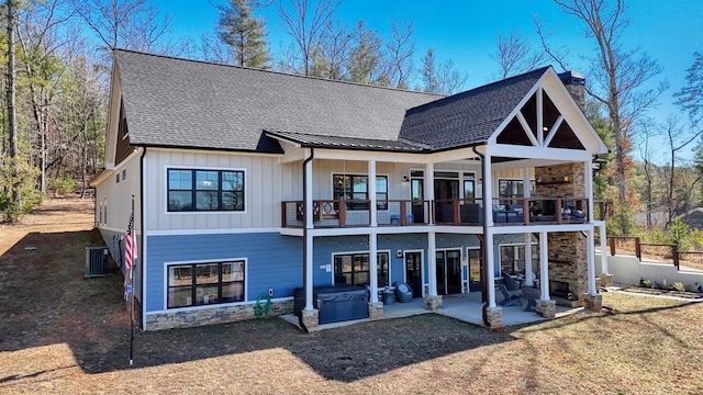 back of house with a hot tub, a patio, a balcony, a chimney, and board and batten siding