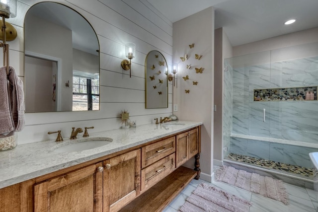 full bath with double vanity, wood walls, a sink, and a marble finish shower