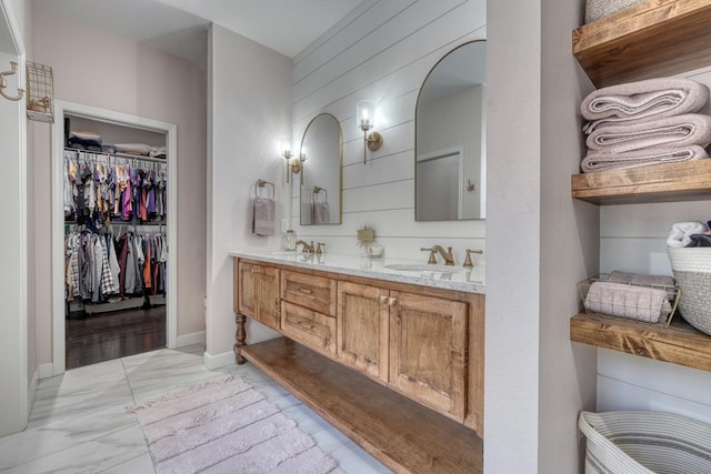 bathroom featuring marble finish floor, double vanity, a sink, wood walls, and baseboards