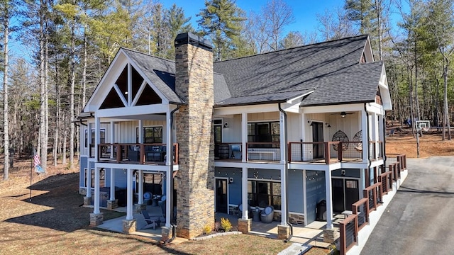 back of property featuring a shingled roof, a chimney, a patio, and a balcony