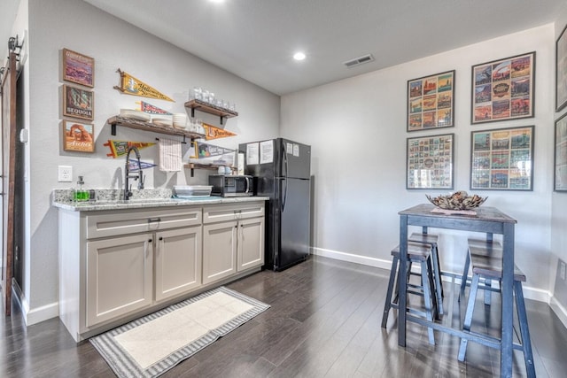 kitchen with freestanding refrigerator, light stone countertops, open shelves, stainless steel microwave, and dark wood finished floors