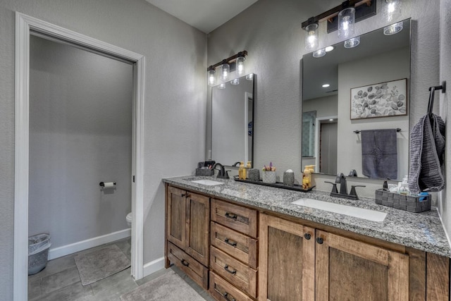 full bathroom featuring double vanity, a sink, toilet, and baseboards