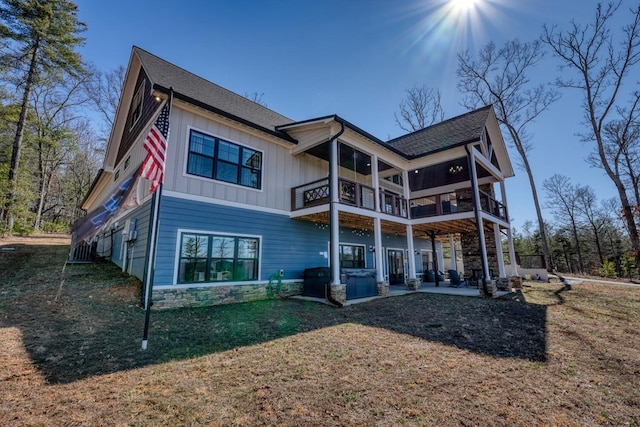 back of property with a lawn, a balcony, stone siding, a patio area, and board and batten siding