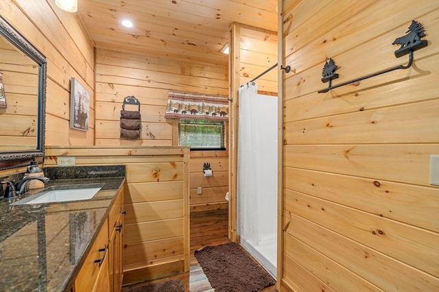 bathroom with vanity, wooden walls, wood-type flooring, curtained shower, and toilet