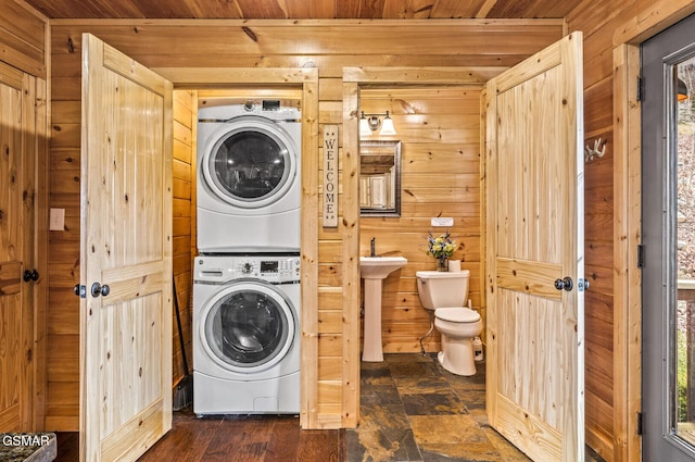 laundry room with wooden ceiling, stacked washer and dryer, wooden walls, and sink