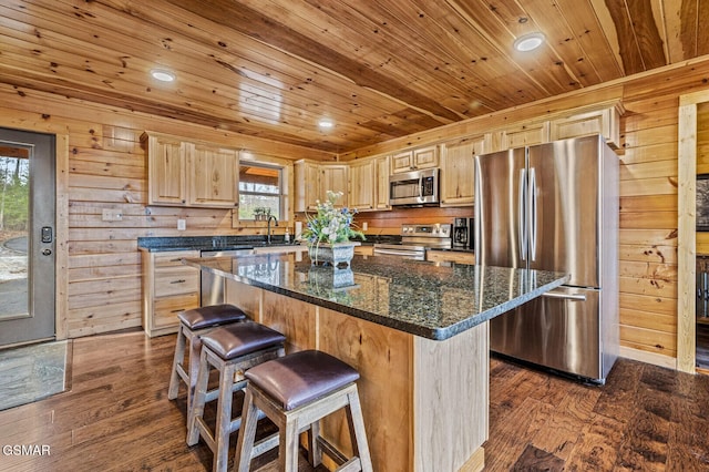 kitchen with wood walls, dark hardwood / wood-style floors, dark stone countertops, a kitchen island, and stainless steel appliances