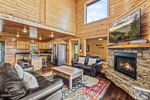 living room featuring a stone fireplace, wooden walls, hardwood / wood-style floors, and a high ceiling