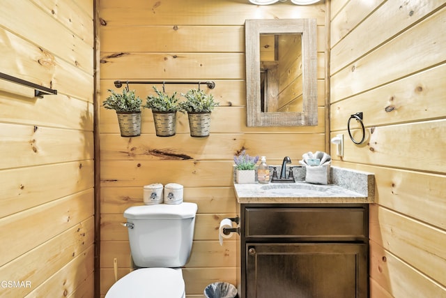 bathroom with vanity, toilet, and wood walls