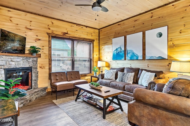 living room with a stone fireplace, wood-type flooring, wooden ceiling, wooden walls, and ceiling fan