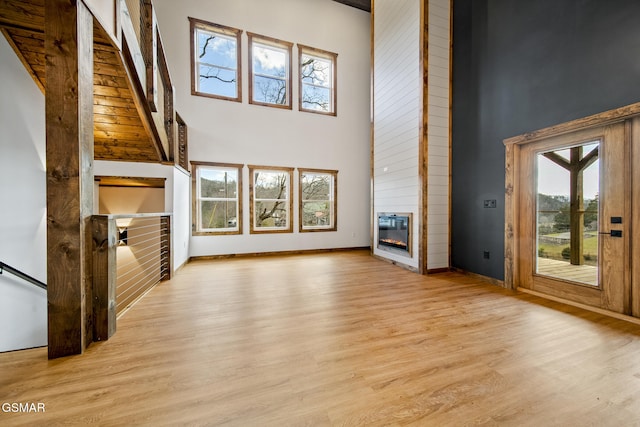 unfurnished living room with a high ceiling, baseboards, light wood-type flooring, and a large fireplace