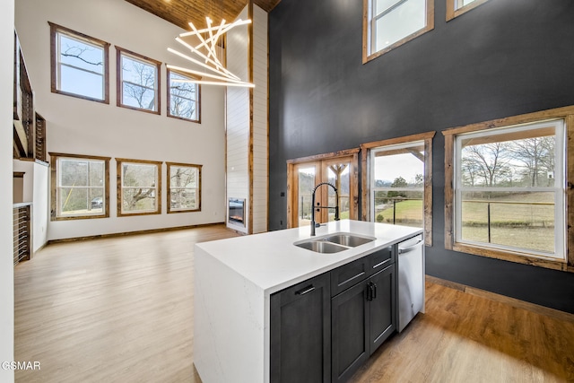 kitchen featuring a sink, light countertops, light wood-style floors, dishwasher, and dark cabinets