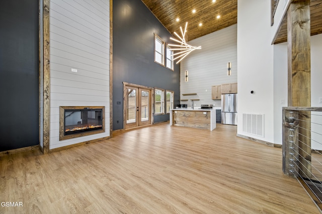 unfurnished living room featuring visible vents, light wood-type flooring, wooden ceiling, french doors, and a glass covered fireplace