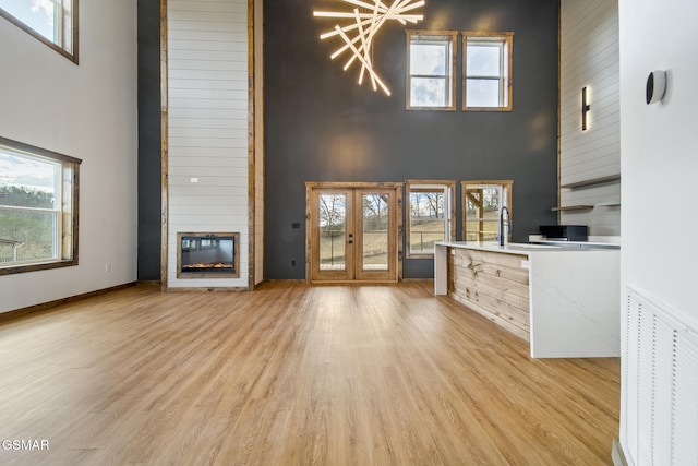 unfurnished living room featuring light wood finished floors, visible vents, french doors, and a large fireplace