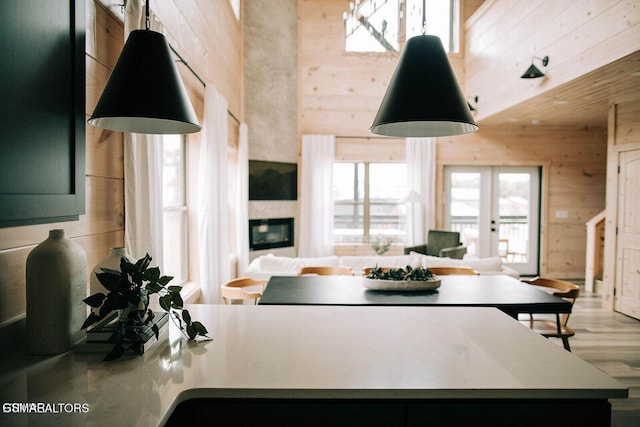 kitchen with french doors, a towering ceiling, light hardwood / wood-style flooring, and wood walls