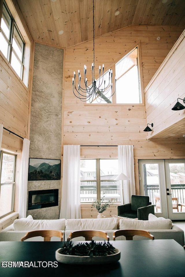 living room featuring a chandelier, high vaulted ceiling, wooden ceiling, a large fireplace, and wooden walls