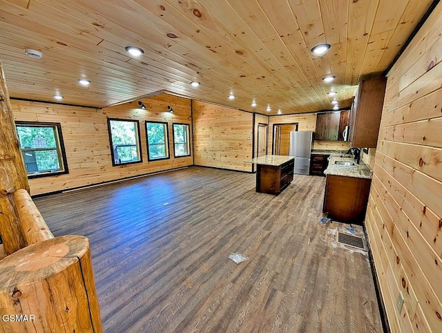 kitchen with stainless steel refrigerator, dark wood-type flooring, wooden ceiling, wooden walls, and a kitchen island