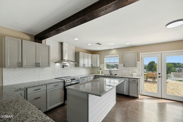 kitchen with french doors, wall chimney range hood, light stone countertops, appliances with stainless steel finishes, and beamed ceiling