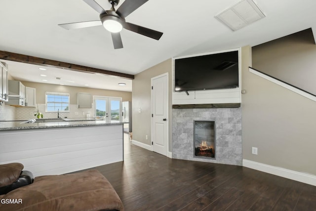 unfurnished living room with a tile fireplace, beam ceiling, dark hardwood / wood-style floors, and ceiling fan