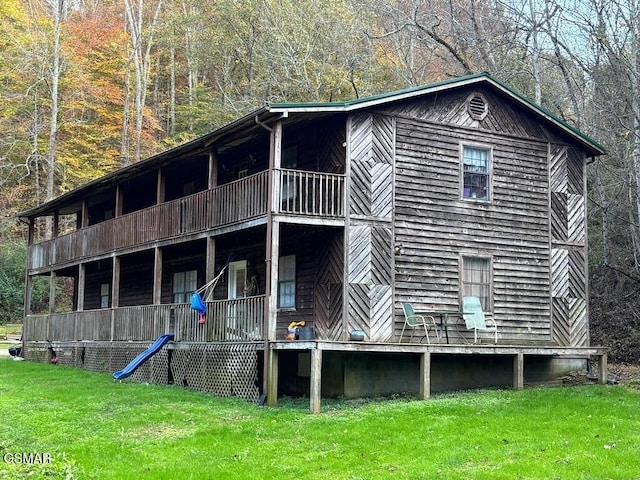 rear view of property with a yard, a balcony, and a forest view