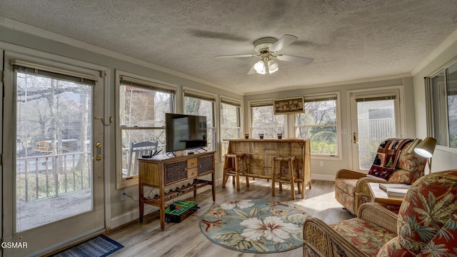 sunroom with a textured ceiling, baseboards, ornamental molding, and wood finished floors