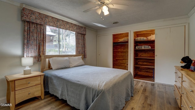 bedroom with two closets, light wood-style floors, and a textured ceiling