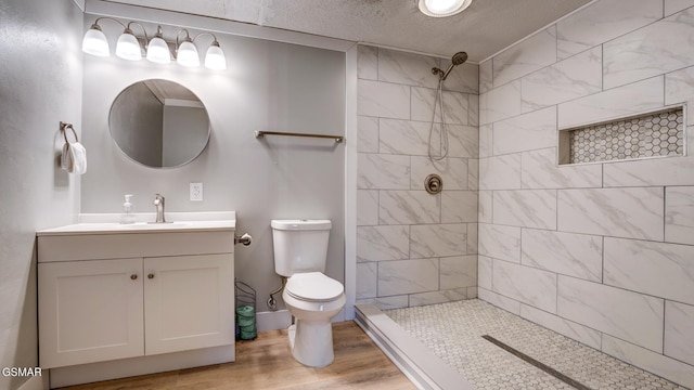 full bath featuring a textured ceiling, wood finished floors, a tile shower, toilet, and vanity