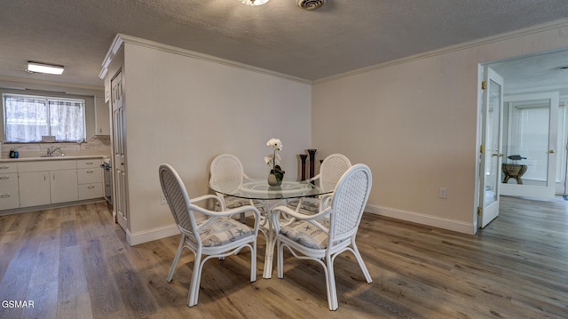 dining space with ornamental molding, baseboards, light wood-style floors, and a textured ceiling
