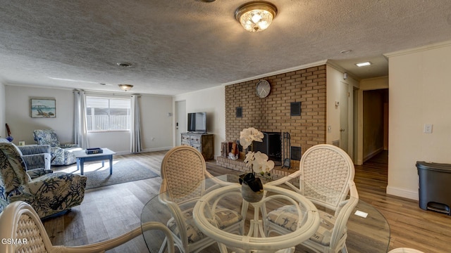 dining space with ornamental molding, wood finished floors, and a brick fireplace