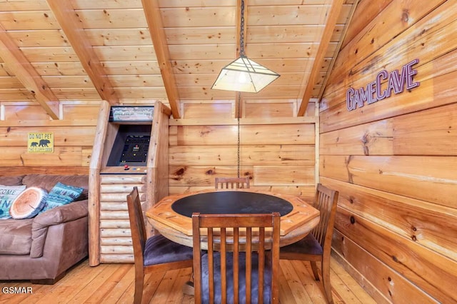 dining area with beam ceiling, wood walls, light wood-style floors, and wood ceiling