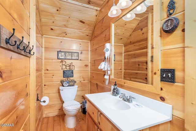 bathroom with wooden walls, toilet, vaulted ceiling, wood finished floors, and vanity
