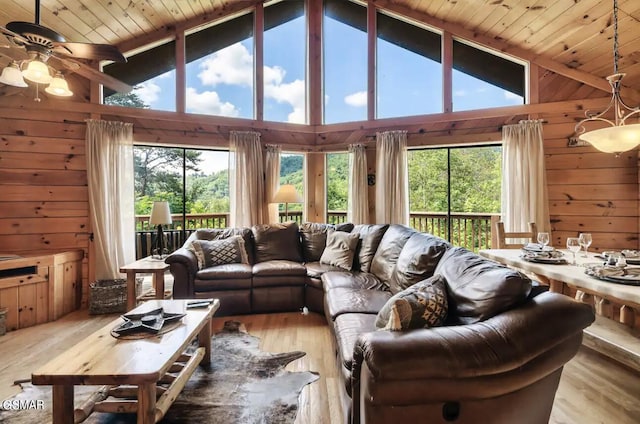 living room with ceiling fan, light hardwood / wood-style flooring, high vaulted ceiling, and wooden walls