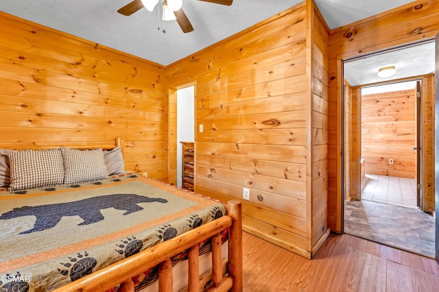 bedroom with ceiling fan, wood walls, wood finished floors, and ensuite bathroom