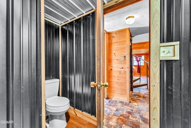 bathroom featuring toilet, wood walls, and stone finish flooring