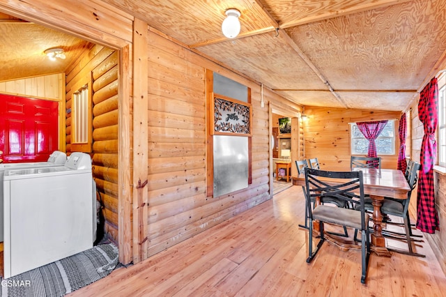 dining room featuring rustic walls, wood finished floors, washing machine and clothes dryer, vaulted ceiling, and wood walls